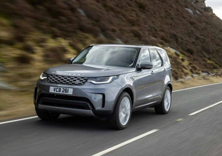 SUV Land Rover Discovery gris foncé en train de rouler sur une route au bord d'une colline