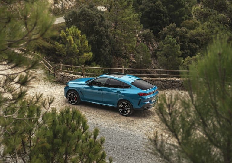 BMW X6 bleu turquoise garé sur le bas côté d'une route de montagne, la photo prend le véhicule de profil afin de bien visualiser la silhouette coupée